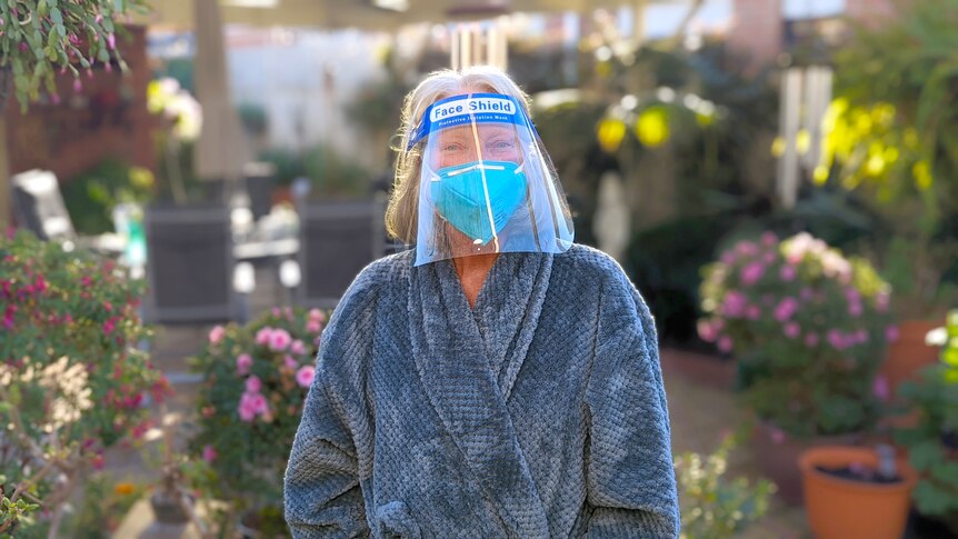 A woman in face mask, face shield and bathrobe in her garden