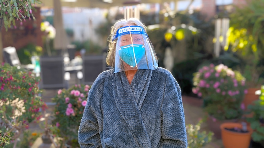 A woman in face mask, face shield and bathrobe in her garden