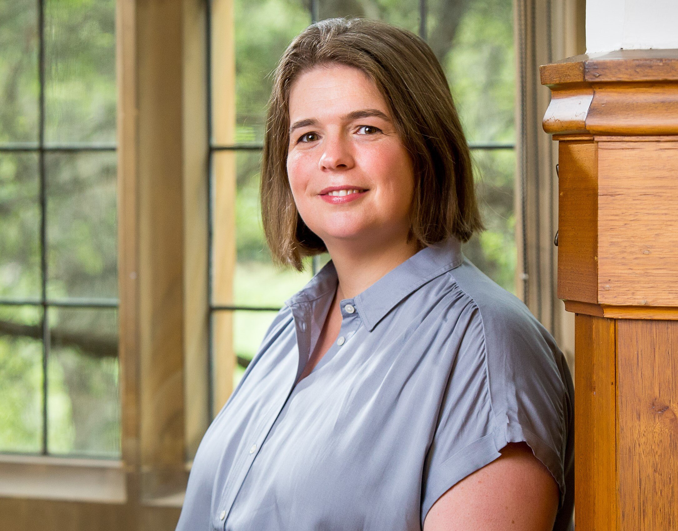 Radha stands in front of glass window panes and wears her brown hair in a bob while smiling
