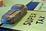 A silver car token sits on a SUPER TAX space on a Monopoly board