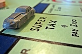 Close-up of a car figurine on a Monopoly board, landing on the "Super tax" square.