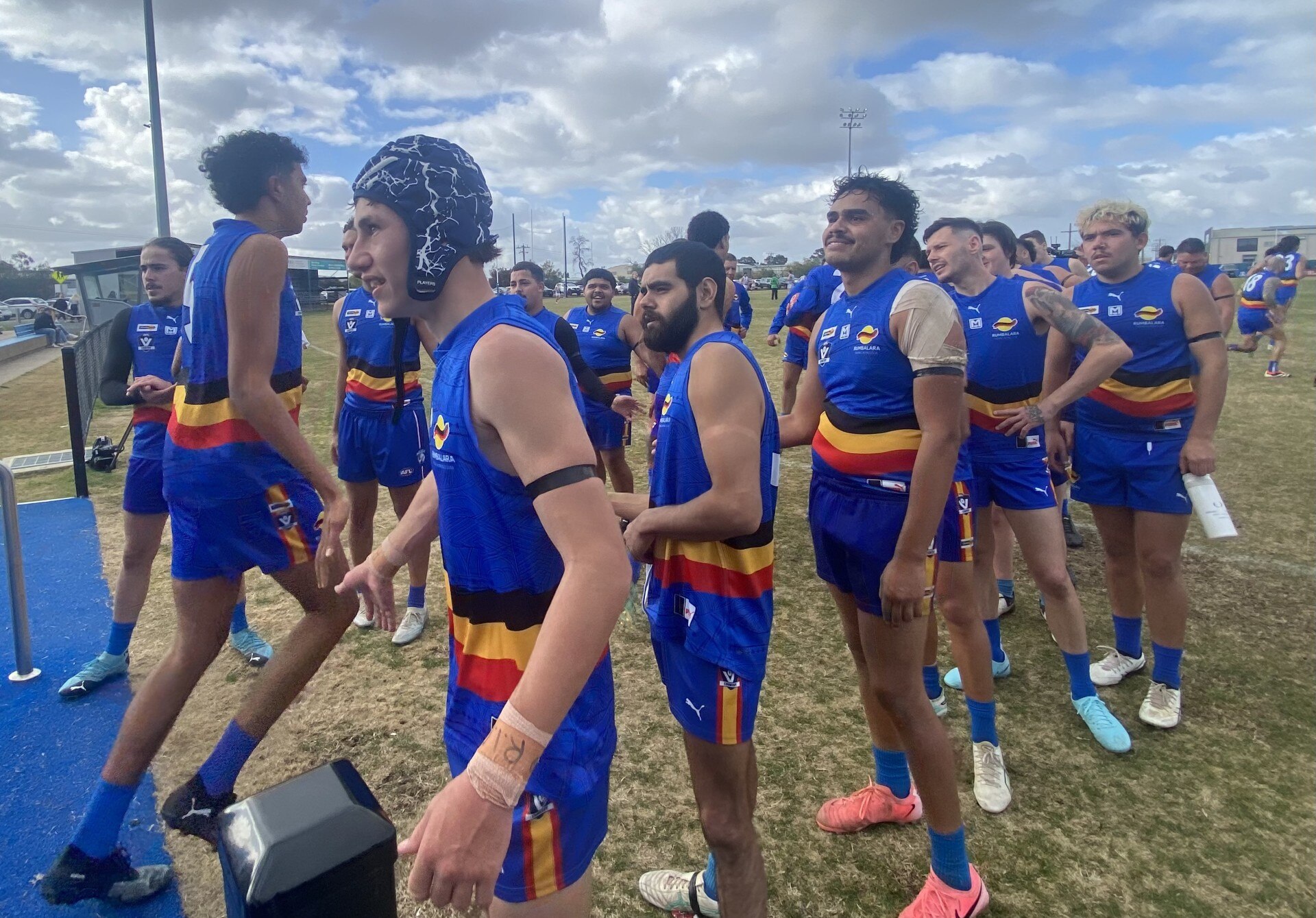 A group of footballers leave the field at a country footy match.