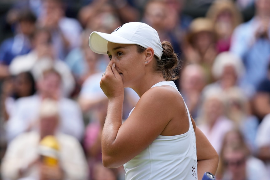 Australian tennis player Ash Barty, wearing all white, puts her hand to her mouth and nose after winning a Wimbledon semi-final.