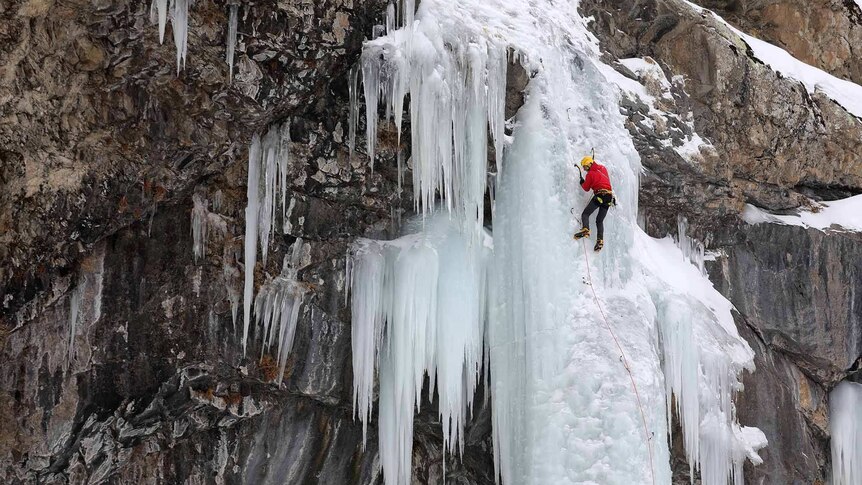 Man climbing frozen waterfall over rocks