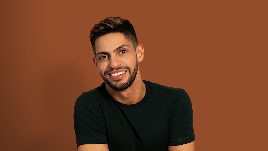 Portrait of comedian and writer AJ Lamarque wearing a black t-shirt and posing in front of a dark orange backdrop.