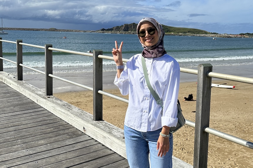 A woman stands on a jetty giving the peace sign