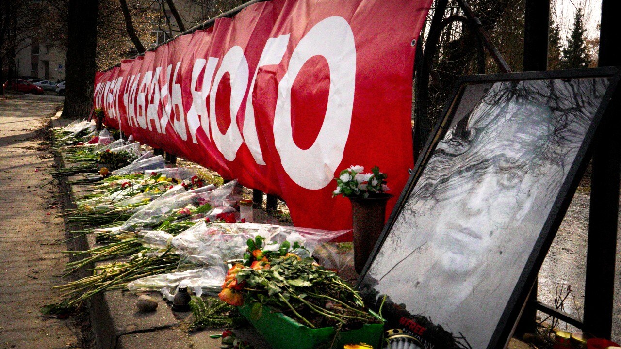 A large photo of a man, near several bunches of flowers.