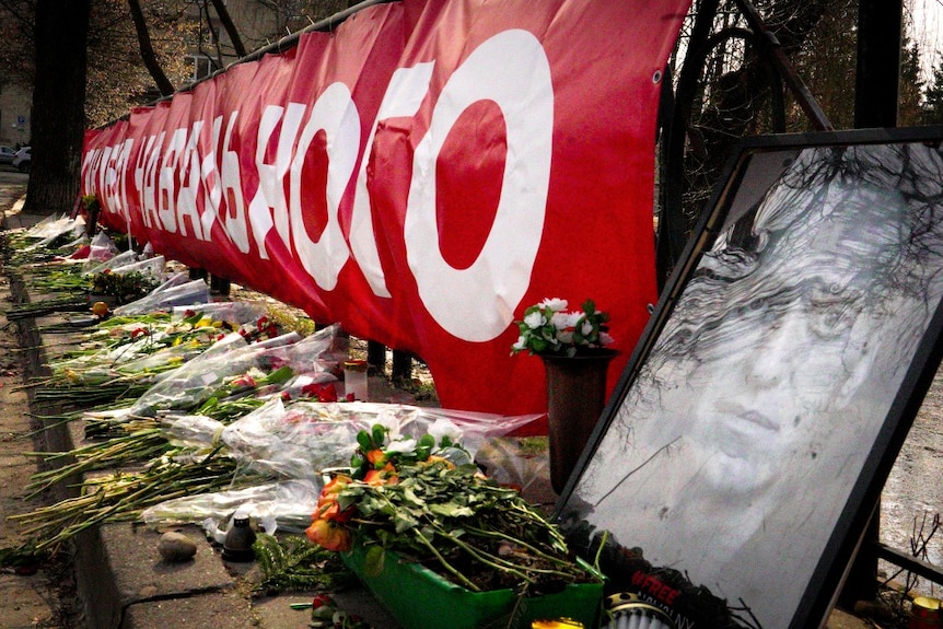 A large photo of a man, near several bunches of flowers.