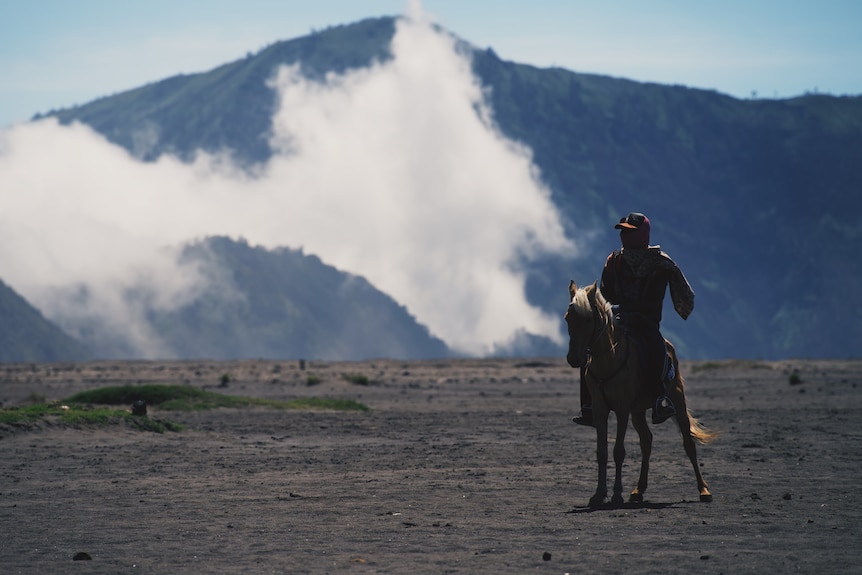 Un hombre a caballo cerca de un volcán.