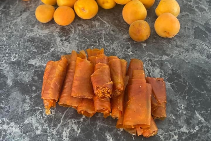 Fresh apricots and homemade apricot fruit straps on a grey marbled kitchen counter.