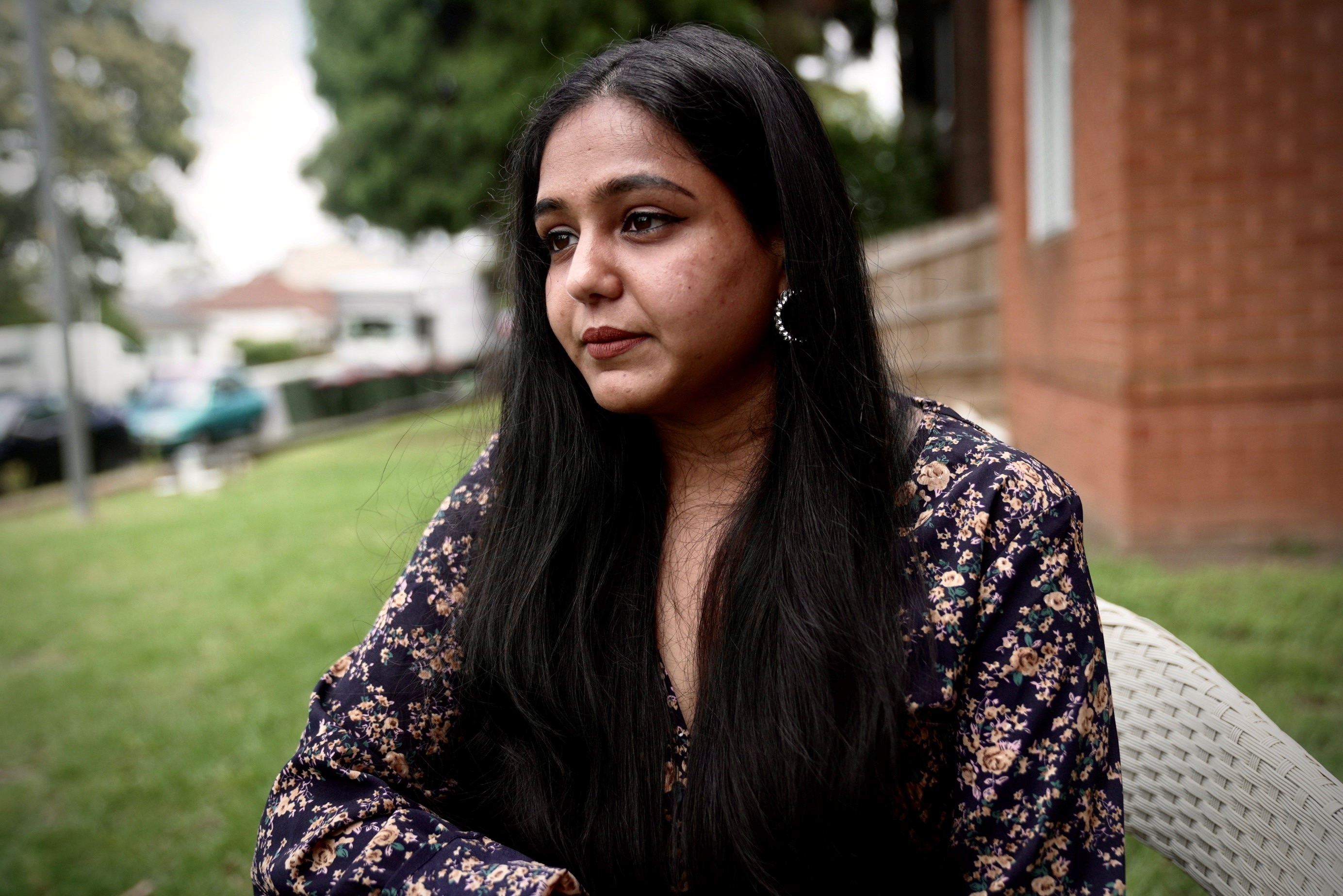 A woman in a floral shirt looking sad in a backyard.
