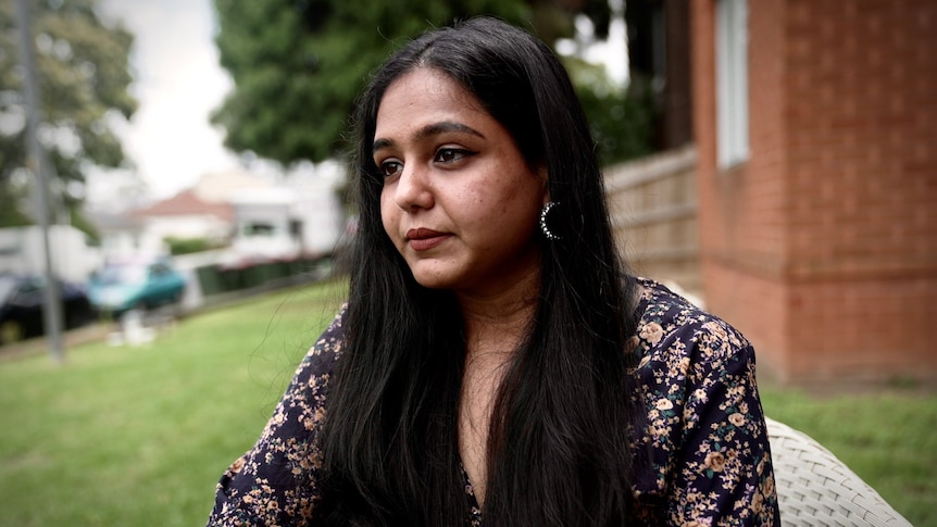 A woman in a floral shirt looking sad in a backyard.