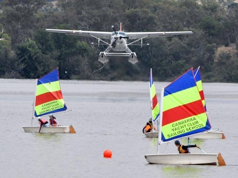 A seaplane lifts off the lake over the top of children in yachts.