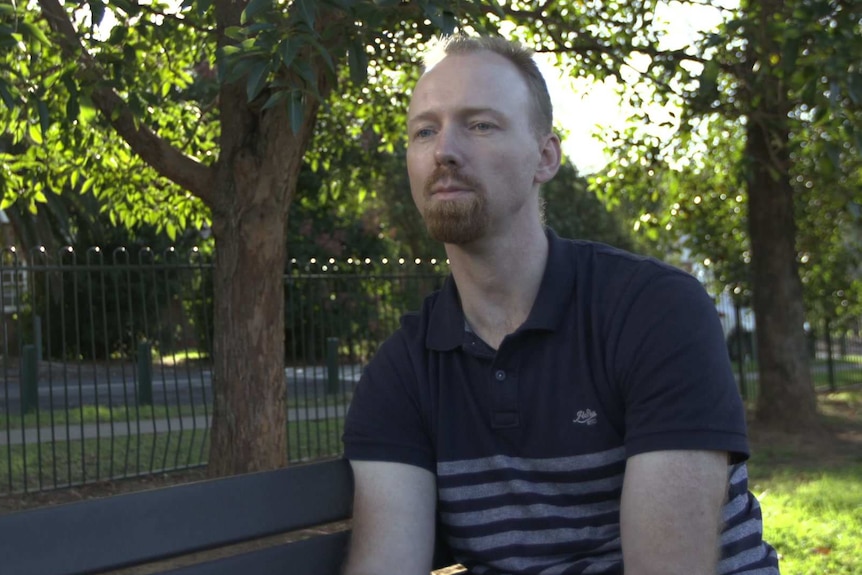 Julian Evans sits in a park, looking to the left of the camera.