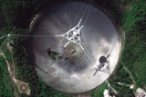 You view a satellite image of a telescope dish with a large hole in it, set within verdant green foliage.