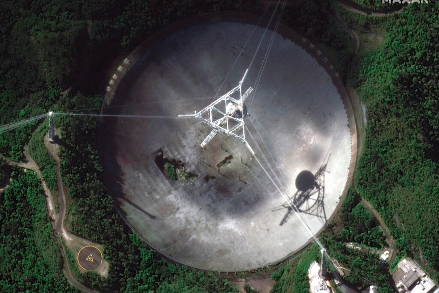 You view a satellite image of a telescope dish with a large hole in it, set within verdant green foliage.