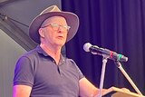 Anthony Albanese wearing a wide-brimmed hat stands at a lectern and delivers a speech at Woodford Folk Festival