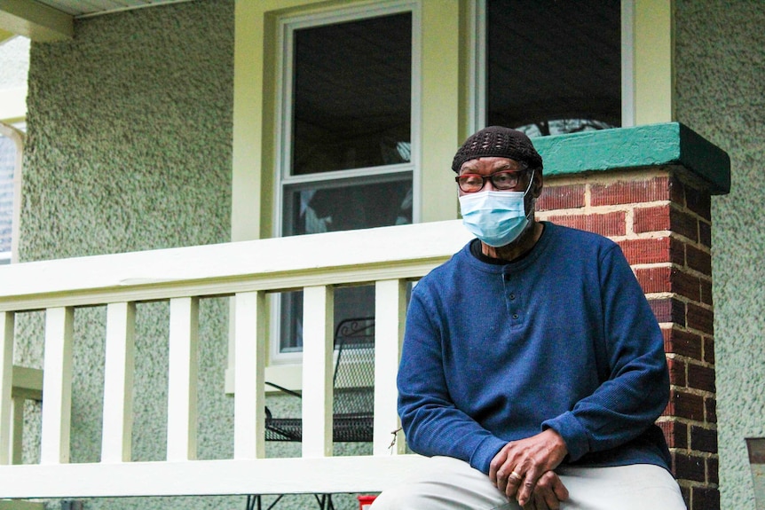 An older African American man in a face mask sits on a porch
