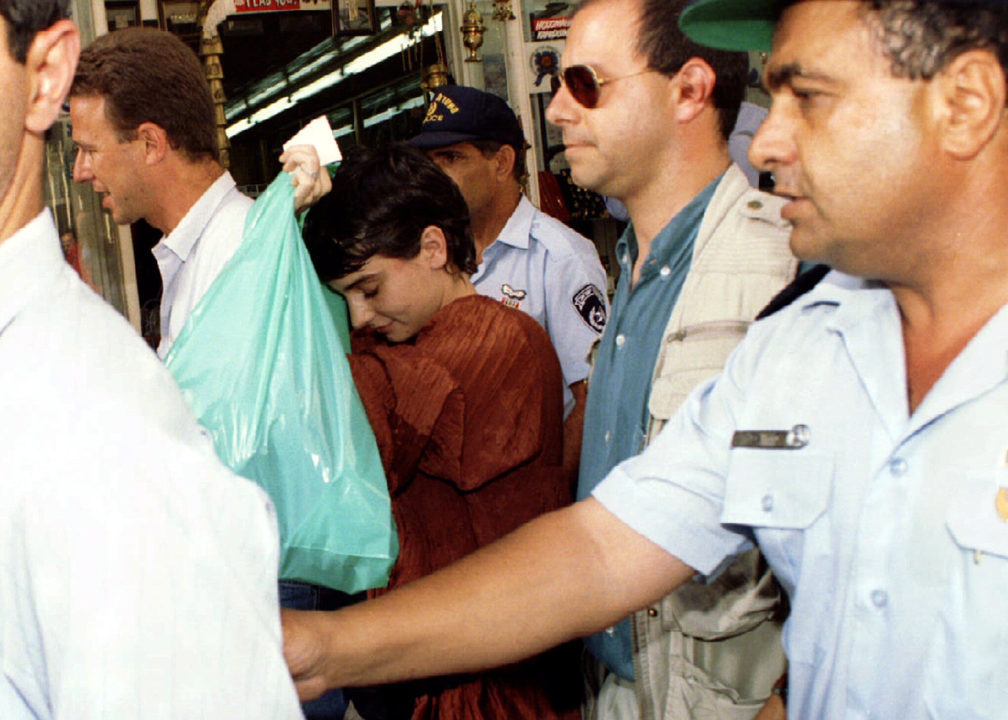 Woman flanked by bodyguards carries a green plastic bag 
