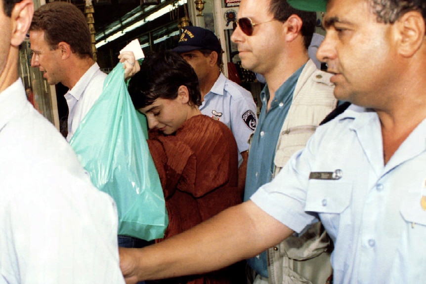 Woman flanked by bodyguards carries a green plastic bag 