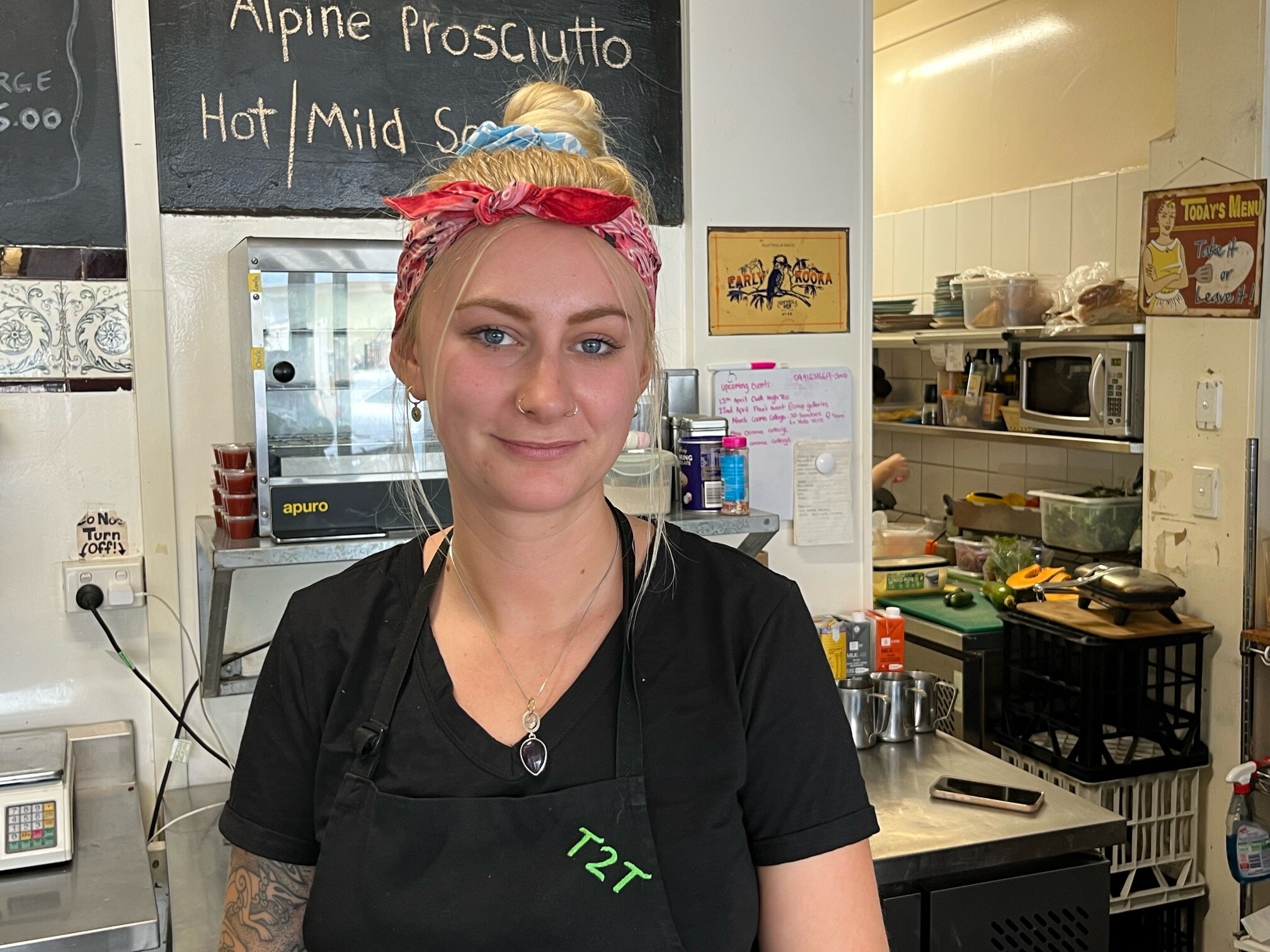 A woman in an apron smiles behind cafe counter
