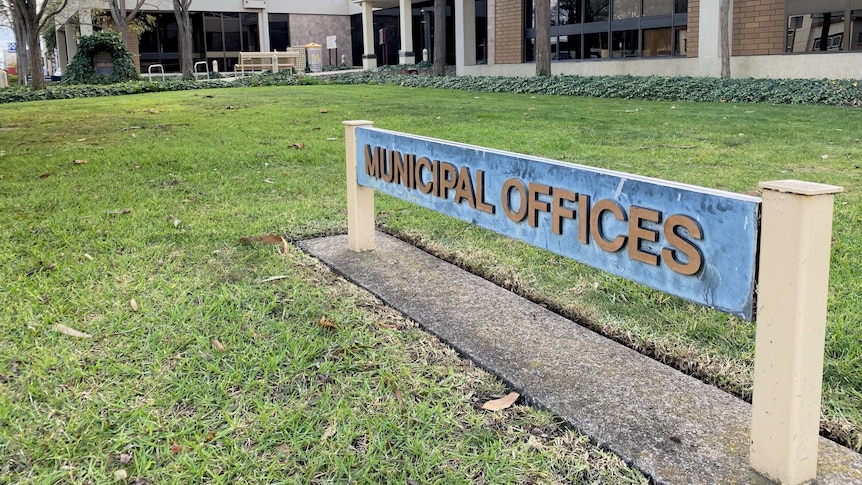A sign that reads "municipal offices", on the grass outside a building.