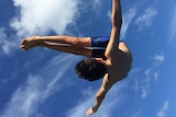 Springboard diver flipping through the air against a blue sky