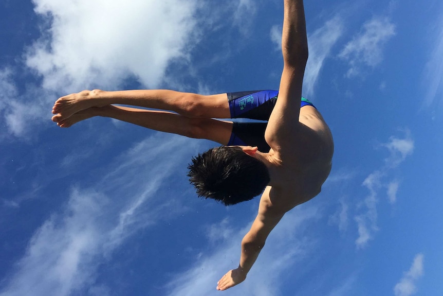 Springboard diver flipping through the air against a blue sky