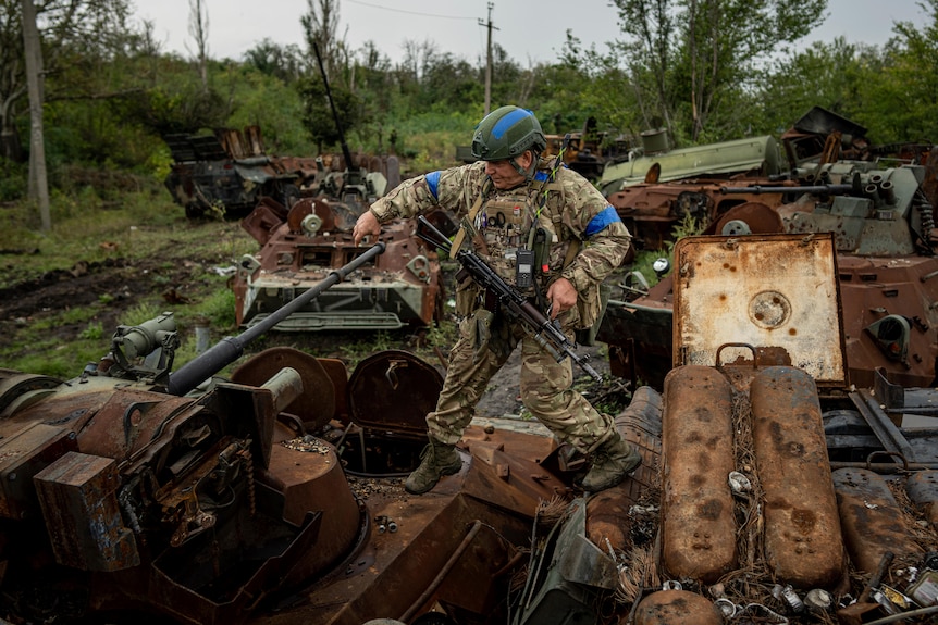 A Ukrainian national guard serviceman walks on the destroyed Russian APC's.
