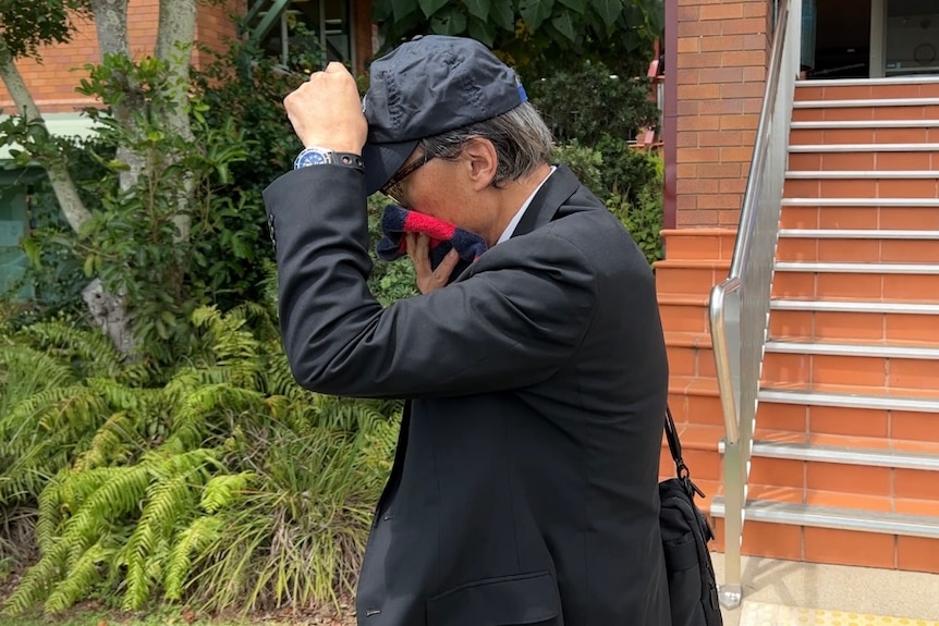 A man in a suit covers his face with a cap and a piece of fabric