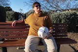 A woman with a turtle neck sweater enjoys the sun on a park bench with a signed soccer ball in her hands, wears dark glasses.