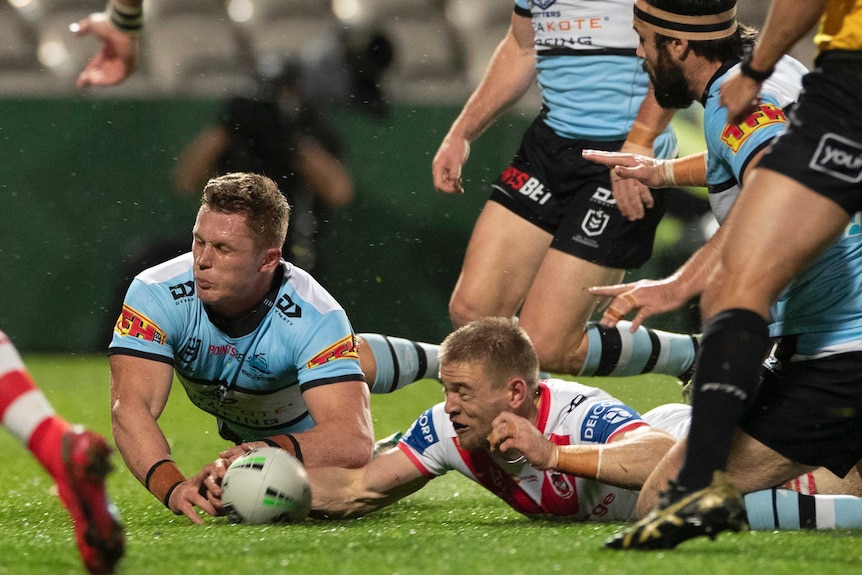 Jack Williams and Matt Dufty dive towards a rugby ball with their eyes closed and arms out