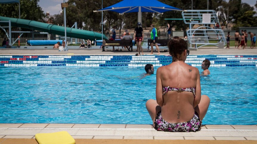 Woman sitting by the side of a public pool in Bendigo, while people swim by