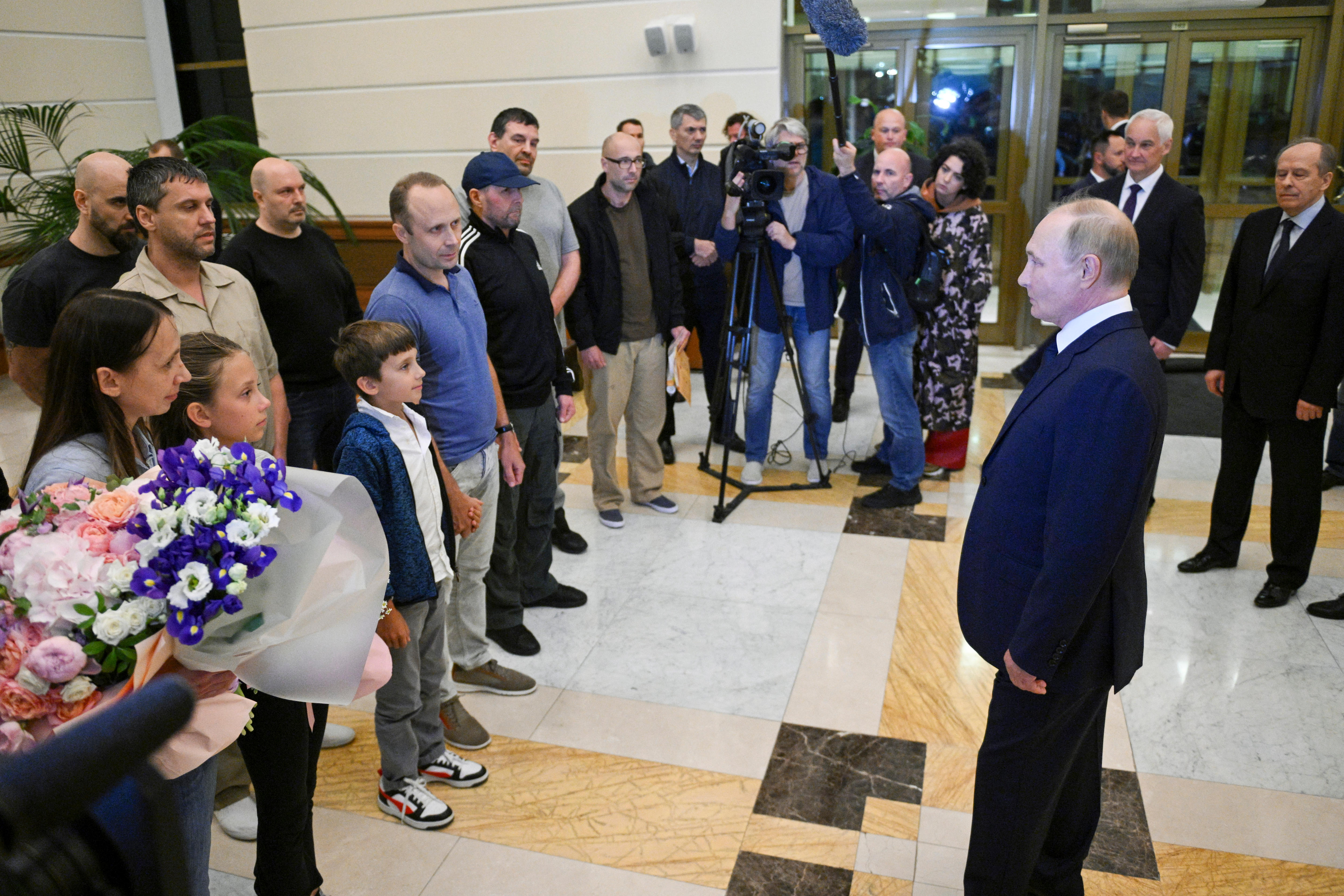 A group of people circle Vladimir Putin in a lobby,