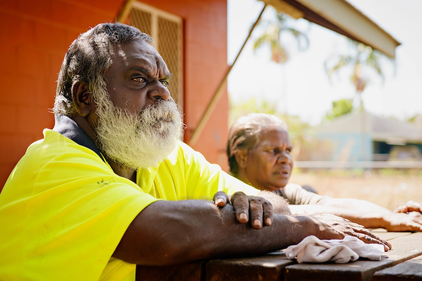 an aboriginal man with a white beard looks into the distance