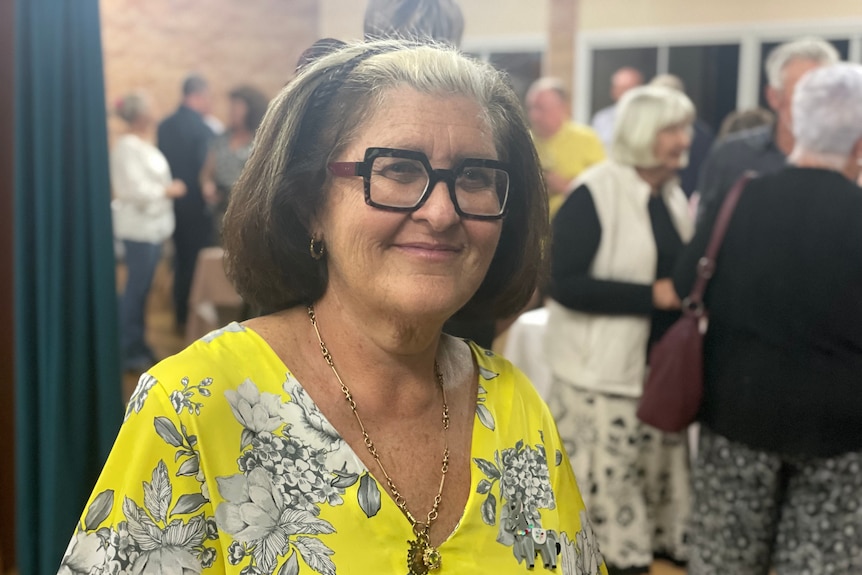 Women in yellow short and thick black lense glasses smiles at the camera 