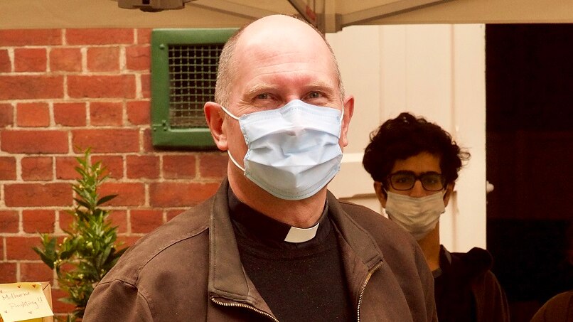 Father Hugh Kempter stands outside a brick building wearing a face mask and jacket.