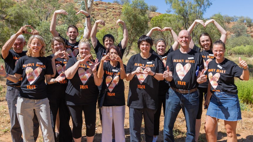 Group of people making heart signs with their arms, wearing black t-shirts.