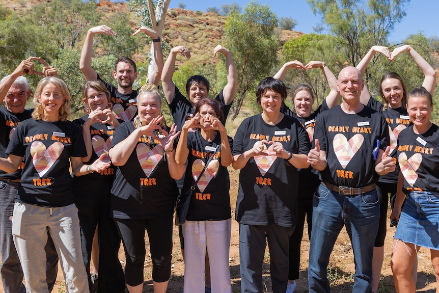 Group of people making heart signs with their arms, wearing black t-shirts.