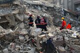 People in search and rescue uniforms stand on rubble.