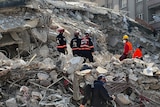 People in search and rescue uniforms stand on rubble.