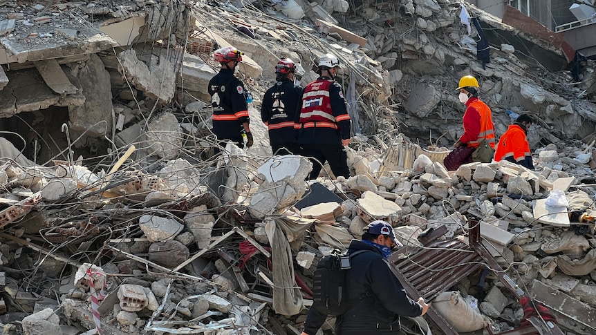 People in search and rescue uniforms stand on rubble.