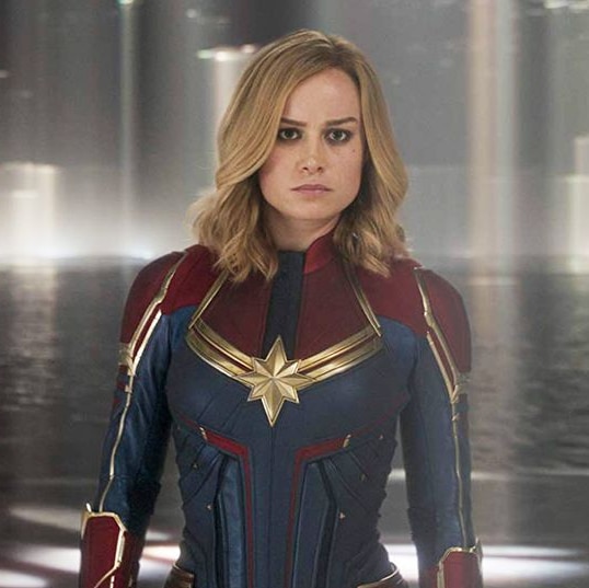 A still from the film Captain Marvel, featuring the main character posing before a pool of water.