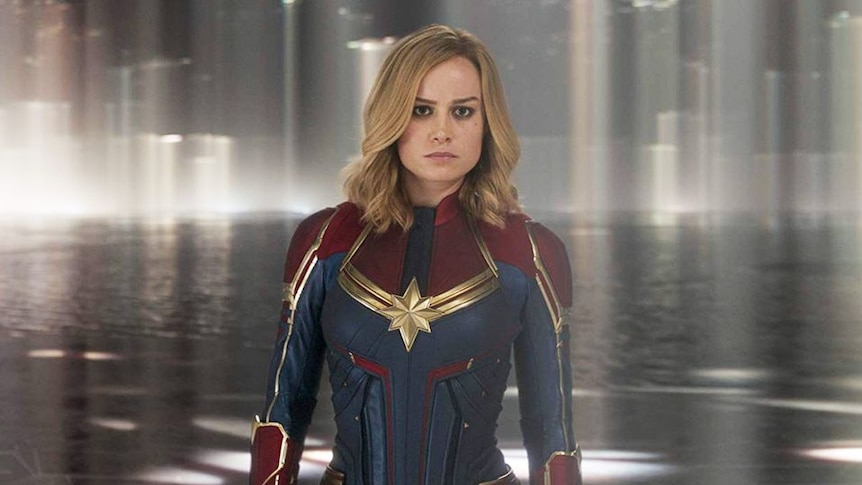 A still from the film Captain Marvel, featuring the main character posing before a pool of water.