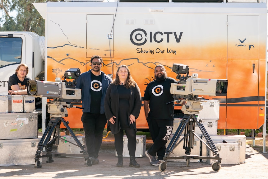 Three men and a woman standing with cameras and equipment in front of a TV van with ICTV on side.