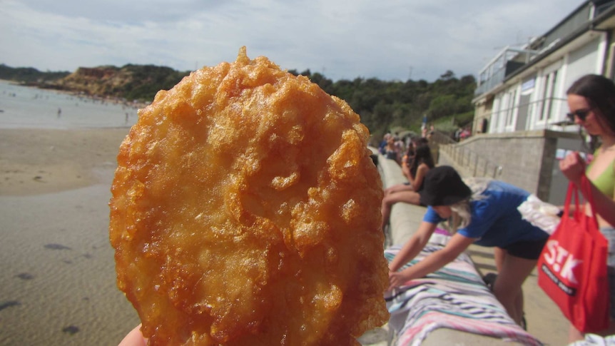 A potato cake being held in someone's hand outside a beach kiosk