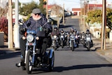 Man riding scooter with pack of motorcyles on road behind him