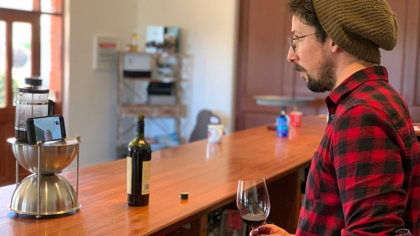 Winemaker Russell Cutting looks at a Zoom meeting on his phone while holding a glass of wine.