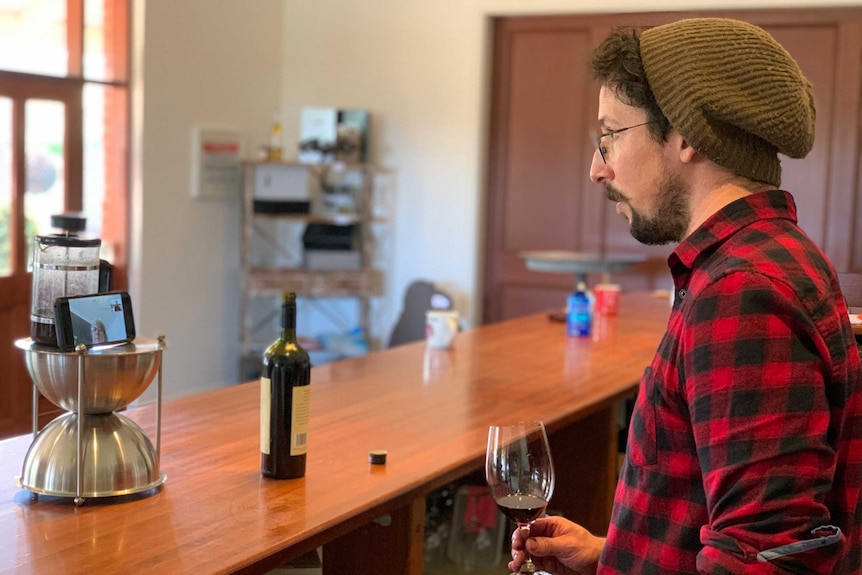 Winemaker Russell Cutting looks at a Zoom meeting on his phone while holding a glass of wine.