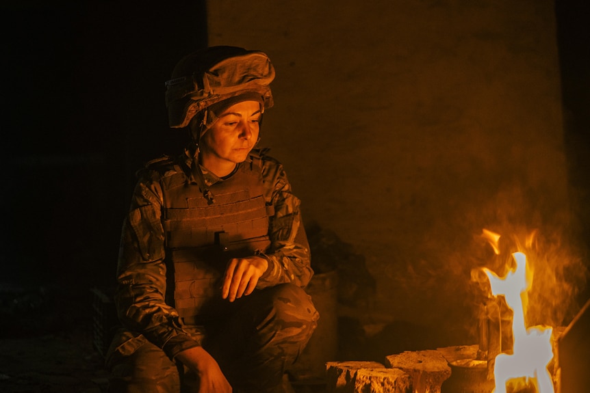 Soldier sits beside small fire.